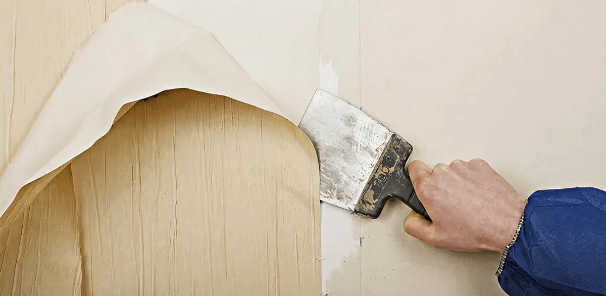Handyman removing wallpaper with a scraper for wall preparation in Nashville, TN